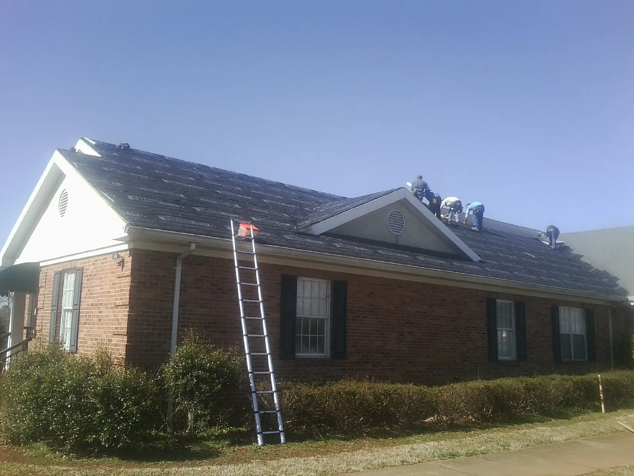 Crew tearing shingles off a brick ranch roof with a ladder set — Metal Roof Repair work by our crew in Wheeler
