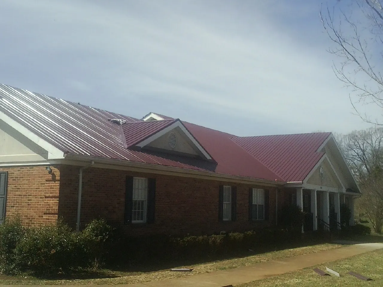 Red metal roof with gabled entries on a long brick building, from a Hail Damage Roof Repair job in Wheeler