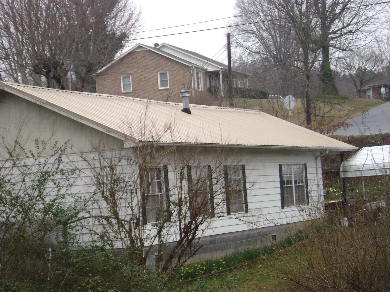 Tan metal roof on a white sided house set into a hillside — Commercial Roofing by Roofing Brothers in Wheeler